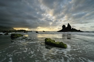 Dramatic cloudy atmosphere with rock formation at rising tide at sunset on the beach of Playa de