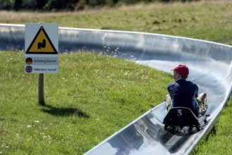 Boy with toboggan on the summer toboggan run, warning sign Attention curve, ski and toboggan arena,