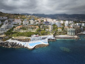 Aerial drone view of Funchal city with hotels resorts and swimming pool along the coast of Atlantic