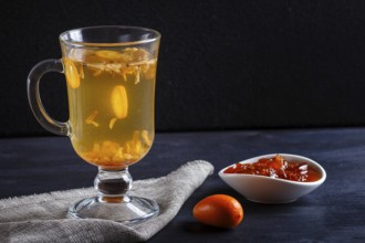 Jasmine tea with kumquat in a glass cup on a wooden board on a black background. close up, copy