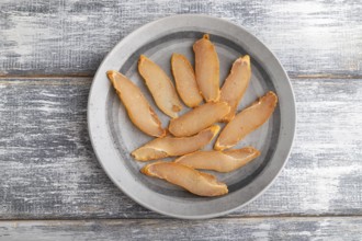 Salted meat on a wooden plate on a gray wooden background. Top view, flat lay, close up