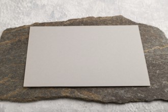 Beige paper business card, mockup with natural stone on gray concrete background. Blank, side view,