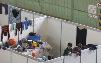 Children of refugees look over the wall of a temporary room in an emergency shelter for refugees on