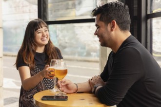 Man and woman enjoying beer in a bar during the day. She is laughing, making it evident that they