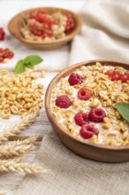 Wheat flakes porridge with milk, raspberry and currant in wooden bowl on white wooden background