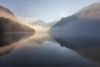 Foggy mood and reflection of mountains in mountain lake, morning light, autumn, Lake Heiterwanger