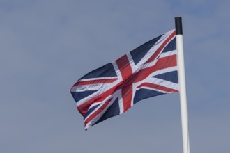 Union jack flag of the United Kingdom blowing in the wind against a blue sky, England, United