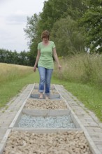 Woman walking barefoot over glass gravel and bottle corks, barefoot path Tilbeck Abbey, Havixbeck,