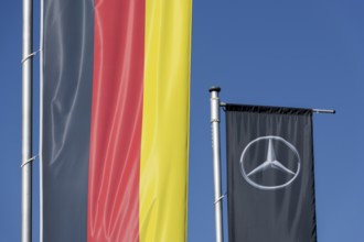 Two flags against a blue sky, one showing the German national colours, the other the Mercedes logo