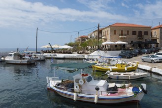 Colourful boats in the harbour next to a coastal town with umbrellas and old buildings, Agios