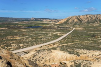 Wide landscape with a long road and hills under a clear blue sky, Bardenas Reales Natural Park,