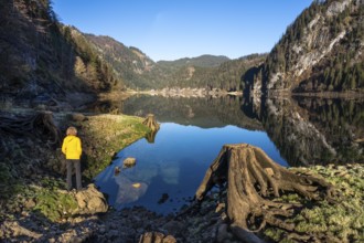 The Vordere Gosausee in autumn with a view of the Gasthof Gosausee. A hiker stands by the lake. A