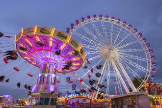 A lively funfair at dusk, illuminated by a large Ferris wheel and a colourful chain carousel,