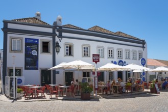 Café with umbrellas and guests outside in front of a blue-painted building on a sunny day, Faro