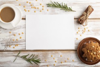 White paper sheet mockup with cup of coffee and cake on white wooden background. Blank, top view,