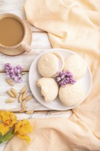 Meringues cakes with cup of coffee on a white wooden background and orange linen textile. Top view,