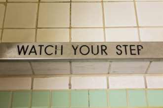 Top view of engraved Watch Your Step black lettering on chrome steel step of shower stall with