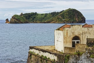 An old ruin on a rocky coast overlooking the sea and the small island and protected area of Ilhéu