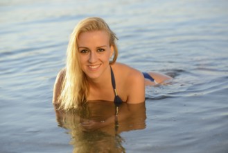 Blonde woman smiling while swimming in the lake, wearing a blue bikini, enjoying the summer,