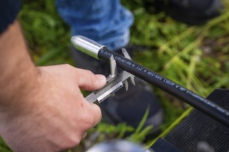 A person checks a black cable outdoors with a caliper gauge, fibre optic installation, Calw