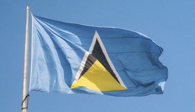 The flag of St Lucia, Caribbean, flutters in the wind, isolated against a blue sky