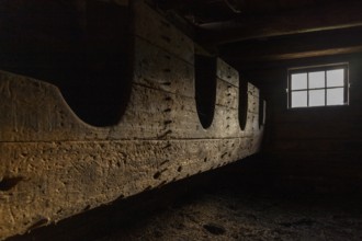 A gloomy stable room with a manger and light streaming in through a window, Neukirchen am