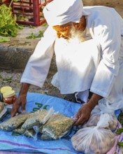 An elderly Omani man in traditional dress offers his wares on the street, weekly market market in