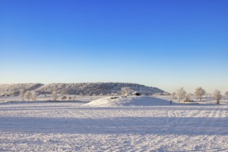 Passage grave from the stone age on a hill at a snowy field in a cold winter landscape at the