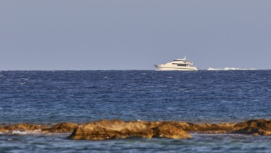 Luxury yacht sailing on the horizon over the blue sea with rocky coast, windsurfer, Meltemi