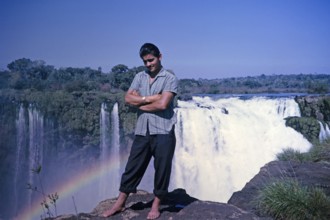 Male tour guide standing barefoot at the edge of the Iguazu Falls on the Iguazu River, on the