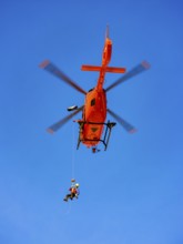 Mountain rescuer of the Bavarian Mountain Rescue Service being winched by the on-board mechanic of