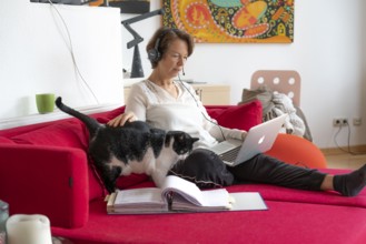 Woman, mid-50s, works from home, with laptop and communicates with colleagues via headset, home