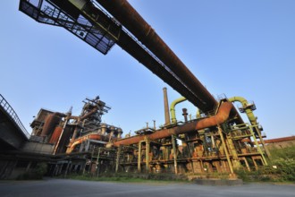 Abandoned industrial site with rusty pipes and dilapidated factory buildings under a clear blue