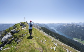 Mountaineer at the summit of Hochunnütz with summit cross, behind Achensee and summit of