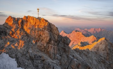 Summit of the Zugspitze with golden summit cross, alpenglow at sunset, Northern Limestone Alps,