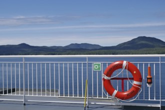 View of the sea from a ship with a lifebuoy and mountains in the background under a clear sky, BC