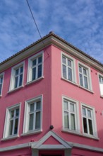 Historic building with pink facade and white window frames under a blue sky with light clouds,