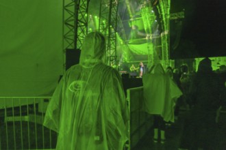 Person in green rain poncho at a night concert with green stage lighting, Klostersommer, Calw