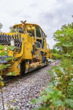 Yellow locomotive on rails, surrounded by trees and foliage, tamping machine, Hermann Hessebahn,