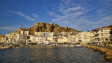 Harbour town with colourful houses by the sea, rocky mountains rise in the background under a blue