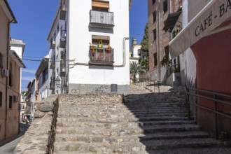 Cobbled cobblestone street with steps and traditional buildings under a blue sky, Granada