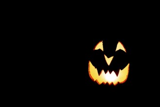 Glowing pumpkin face, Halloween, against a black background