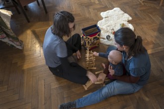 Young mother with her sister and with her son, 8 months, playing on the parquet floor,