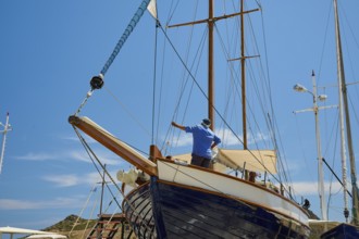 A man repairs the wooden sailing boat at the mast under a blue sky, Patmos Marine, boatyard,