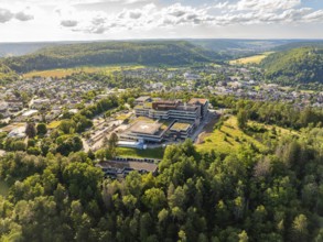 Aerial view of a building in the middle of a green forest, surrounded by an urban landscape under a