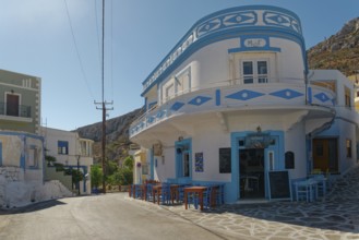 Blue and white café on a street corner of Menetes with colourful tables and chairs under a clear