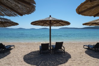 Sunny beach with deckchairs under straw umbrellas. Turquoise sea with islands in the background,