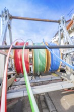 Coloured cables on a large reel in front of a building background, Wend Glasfasermontage during the