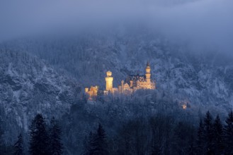 A fabulously illuminated castle lies in the snow-covered mountains in the evening mist,