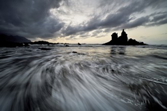 Dramatic cloudy atmosphere with rock formation at rising tide at sunset on the beach of Playa de